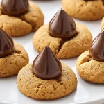 A batch of freshly baked Peanut Butter Kiss Cookies with a Hershey's chocolate kiss on top, arranged on a cooling rack.